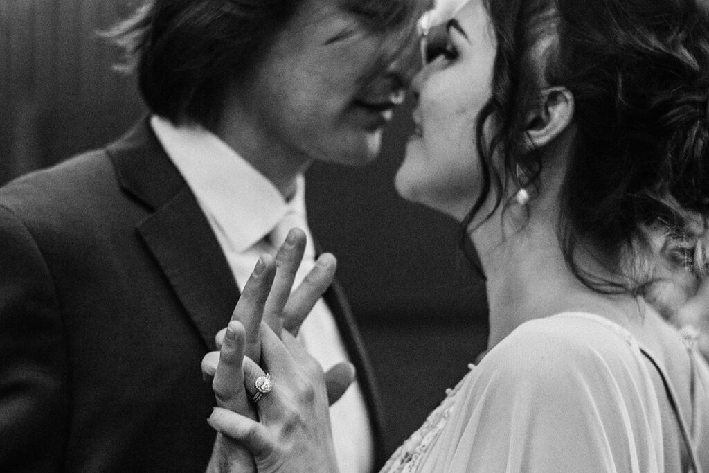 a bride and groom holding hands and almost kissing. the image is cropped tightly and is in black and white